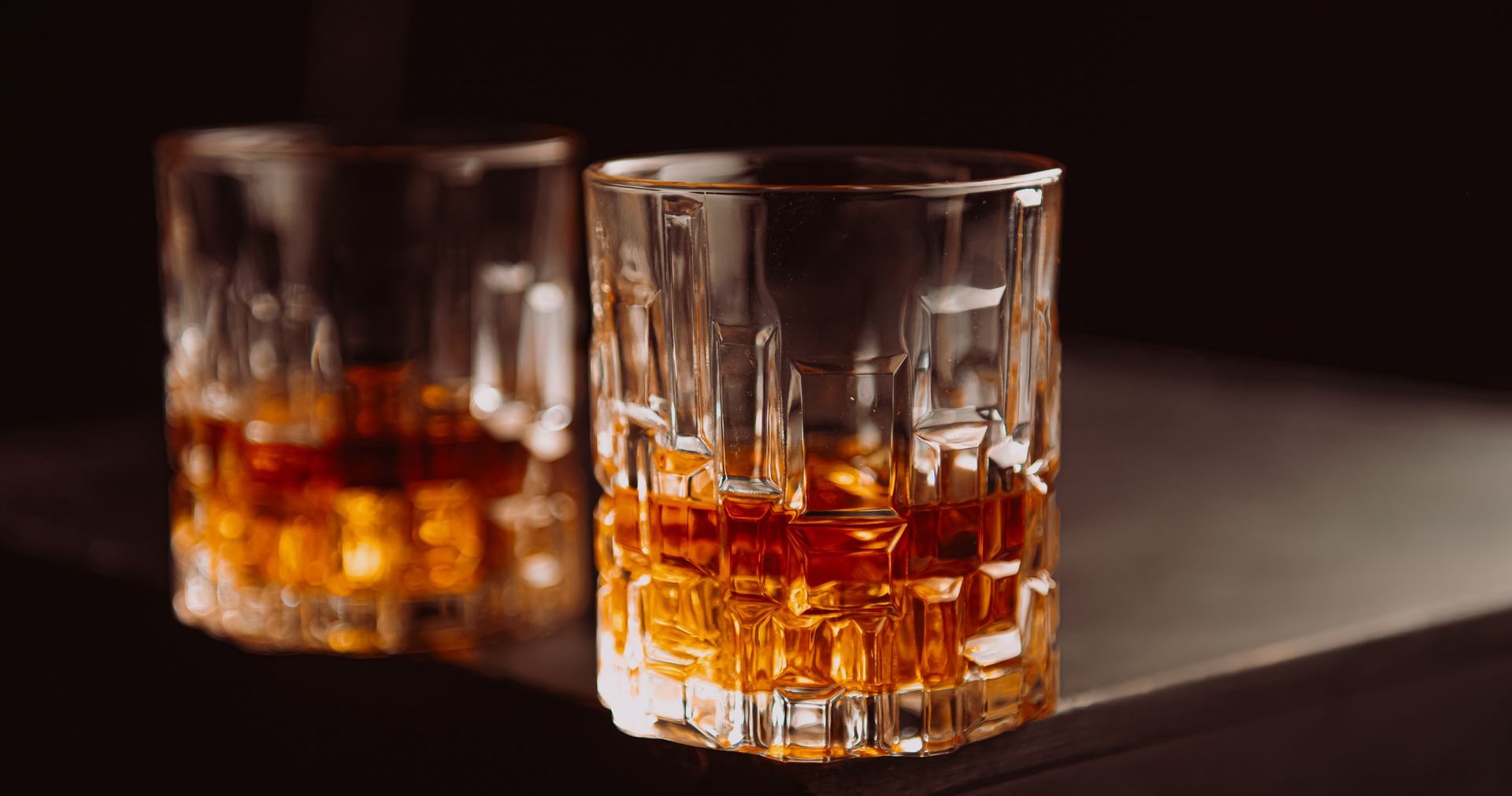 Two glasses of whisky on a dark counter